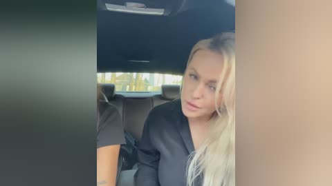 Media: Video of a blonde woman with long hair, wearing a black top, sitting in a car, looking pensive.