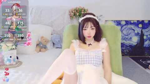 Media: A video of an Asian woman with short dark hair, wearing a plaid crop top and white thigh-high stockings, sitting in a cozy room with a green chair, floral background, and a stuffed bear.