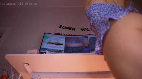 Media: Video of a woman's bare back, wearing a blue and white patterned bra, in a room with a computer desk displaying multiple computer screens, with a \"SUPER WORLDS\" banner in the background.