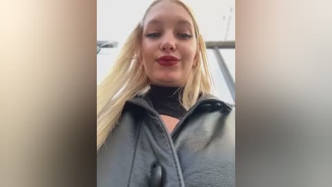 Media: A video of a blonde woman with a fair complexion, wearing a black leather jacket, smiling slightly, taken from a low angle.