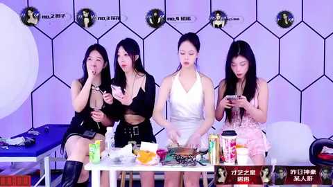 Media: Video of four East Asian women in casual, revealing outfits, seated at a cluttered table, against a white hexagonal-patterned backdrop. They are engaged in conversation, holding cups and snacks.