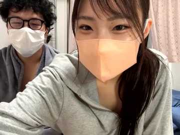 Media: Video of two Asian people wearing surgical masks and gray hoodies, one with glasses and curly hair, the other with straight hair, in a hospital setting.