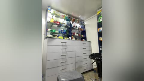 Media: Video of a small, organized bedroom with a gray dresser, shelves of colorful toys, a black chair, and a gray stool.