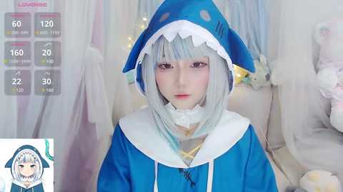 Media: Video of a young woman wearing a blue shark costume with a white collar, indoors with a soft, pastel background and a game screen overlay.