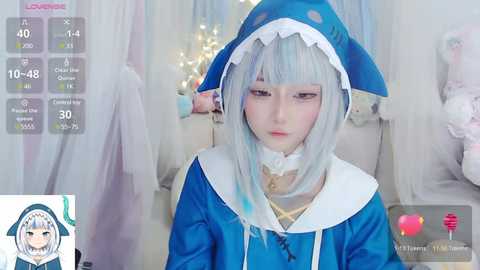 Media: Video of a pale-skinned person with light blue hair in a shark costume, wearing a white choker, in a softly lit room with white curtains. The background shows a virtual live-stream overlay.