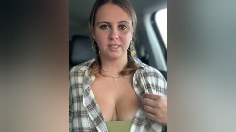 Media: Video of a smiling, light-skinned woman with brown hair in a plaid shirt, revealing cleavage, inside a car with blurred background.