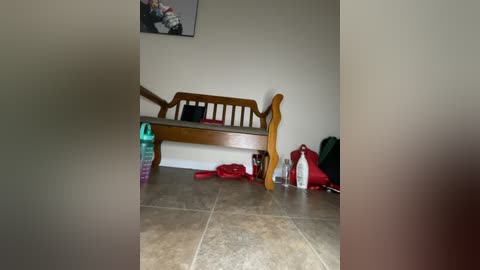 Media: A video of a cluttered, small room with a wooden bench against a plain wall, surrounded by scattered toys, a red bag, and a bottle on the tile floor.