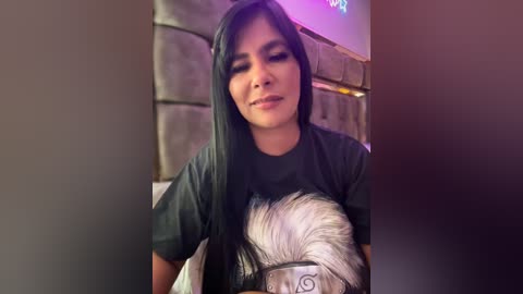 Media: Video of a young woman with long, straight black hair, wearing a dark T-shirt with a white, graphic design of a wolf's head, sitting indoors.