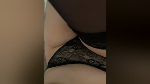 Media: A close-up video of a person wearing black lace panties, with a focus on the groin area and thighs. The background is a muted, warm-toned gradient. The image has a sensual, intimate feel.