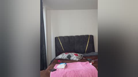 Media: Video of a minimalist, unmade bed with a dark brown, tufted headboard and a pink towel, set against a plain white wall.