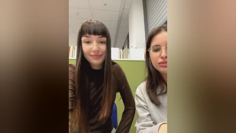 Media: Video of two young women in a library; one with long brown hair and brown sweater, the other with straight brown hair and glasses, both smiling.