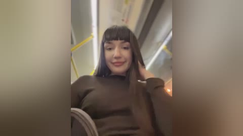 Media: A video of a smiling woman with long black hair, wearing a black sweater, seated on a yellow and gray subway train, looking straight ahead.