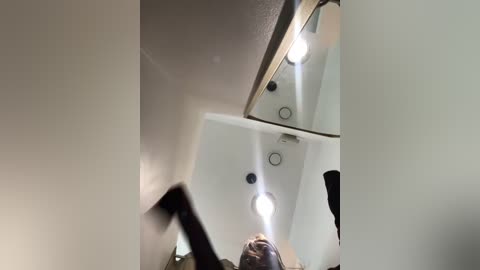 Media: A video of a person, likely a man, standing in a mirror, with the reflection capturing a dimly lit, modern bathroom with a white ceiling and recessed lighting.