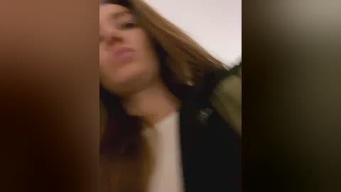 Media: A blurred, close-up video of a woman with long brown hair, wearing a black leather jacket over a white top, captured from an unusual, low-angle perspective.