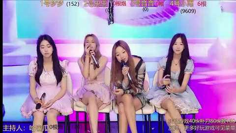 Media: Video of four East Asian women in pastel dresses, seated on chairs, singing into microphones against a colorful, abstract backdrop.