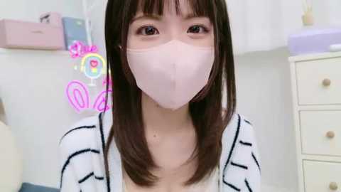 Media: Video of an Asian woman with straight, shoulder-length dark brown hair, wearing a white mask, white and black striped cardigan, and light makeup, in a brightly lit, minimalist room with pink and purple neon lights.