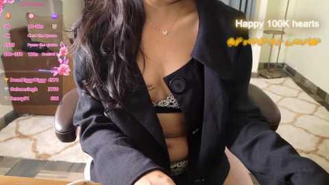 Media: Video of a woman in a black coat, revealing a leopard-print bra, sitting at a desk. Background includes a pink and white flower arrangement, and a \"Happy 100k\" message.