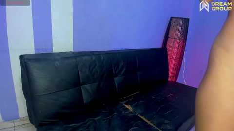 Media: Video of a modern living room corner with a black leather couch against a blue wall. A tall, striped red and black floor lamp stands beside it, casting shadows.