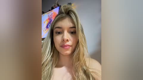 Media: Video of a young woman with long, blonde hair, fair skin, and light makeup, wearing a colorful, floral headband, standing against a plain, light-colored wall.