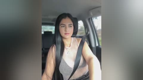 Media: Video of a young woman with long black hair, wearing a sheer, patterned top, seated in a car, with the car's interior visible.