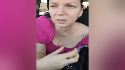 Media: Video of a middle-aged woman with short brown hair, wearing a pink top, adjusting her bra inside a car, with pink vertical filters obscuring parts of the image.