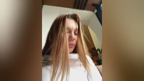 Media: Video of a young Caucasian woman with long, straight blonde hair, wearing a white sweater, sitting indoors, possibly in a hair salon.