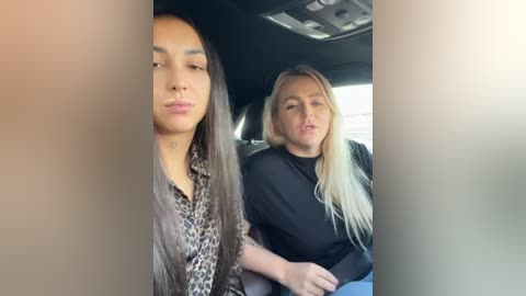 Media: Video of two women in a car; one with long, straight, dark hair, wearing a leopard-print blouse; the other with long, straight, blonde hair, wearing a black top. They appear relaxed, possibly taking a selfie.