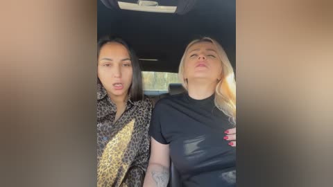 Media: Video of two women seated in a car, one with long dark hair in a leopard print shirt, the other with blonde hair in a black shirt, both with neutral facial expressions.