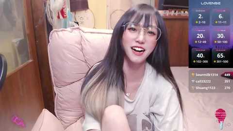 Media: A video of a young Asian woman with long black hair and glasses, wearing a white t-shirt, smiling in a cozy living room.