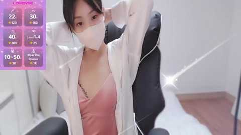 Media: Video of a woman in a white lab coat, pink top, and black leggings, removing a face mask, with a purple background displaying health metrics.