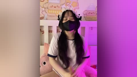 Media: Video of an Asian woman in a cat maid cosplay, wearing a black mask, white t-shirt, and headband, with a pink plush cat beside her, in a pink-themed room.