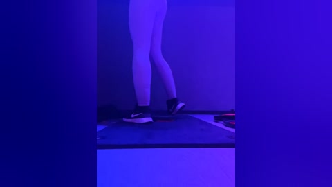 Media: A video of a person in white leggings and black sneakers, standing on a table against a dark background with purple lighting. The setting suggests a minimalist, modern atmosphere.