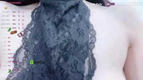 Media: Video of a woman's bare upper chest and neck, adorned with a delicate, gray lace scarf, featuring intricate floral patterns. The background includes a computer screen displaying a calendar and icons, suggesting a virtual setting.