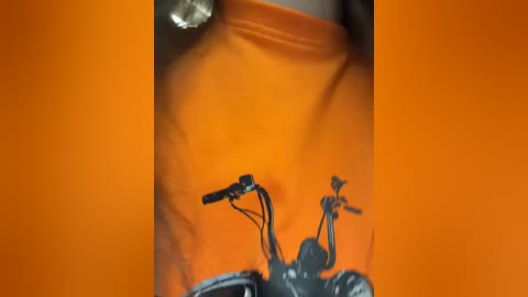 Media: A close-up video of a person's upper torso, wearing a bright orange T-shirt with a black silhouette of two motorcycles on the front. The background is a solid orange color.