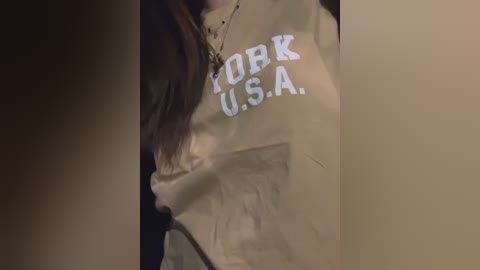 Media: A video of a person wearing a light beige sweater with the word \"KORP USA\" in white text, partially visible. The sweater is slightly wrinkled. The background is dark and indistinct, suggesting an indoor setting.