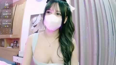 Media: A video of an East Asian woman with long, dark hair, wearing a white face mask, revealing a slender figure and medium-sized breasts, in a bedroom setting with a window, a white hat, and a digital clock visible.