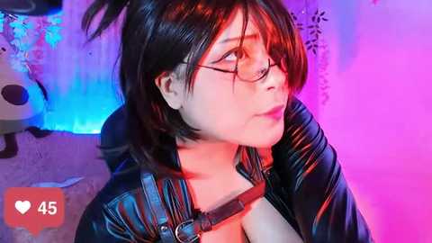 Media: Video of an Asian woman with short black hair, glasses, and a black leather jacket, sitting against a colorful, glowing backdrop.