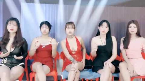 Media: Video of five Asian women in revealing lingerie, seated on red plastic chairs, with bright lights and a plain white background.