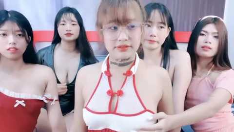 Media: Video of five Asian women, three in red dresses, two in black, posing close together; one woman wears a white halter top with red beads.