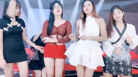 Media: Video of four Asian women in trendy outfits on a stage with white and red lighting. They have diverse styles: black lace top, red crop top, white ruffled skirt, and black floral dress.