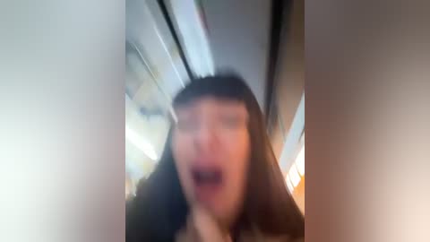 Media: Blurry video of a person with long dark hair, glasses, and a wide-open mouth, possibly in a moving vehicle, with a background of blurred indoor lights.