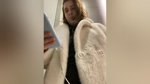 Media: A video of a person with shoulder-length brown hair, wearing a beige coat and a black scarf, taking a selfie with a white stuffed dog.