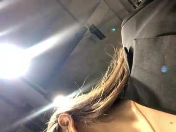 Media: A video captures a person's blonde hair, illuminated by a bright light, being styled in a salon. The backdrop features a textured ceiling and a large, dark hair dryer. The scene is intimate and focused on the hair-styling process.