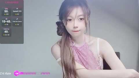 Media: Video of a young Asian woman with long brown hair, wearing a pink lace top, sitting indoors against a plain background. Screen overlay shows \"City Rain\" video game stats.