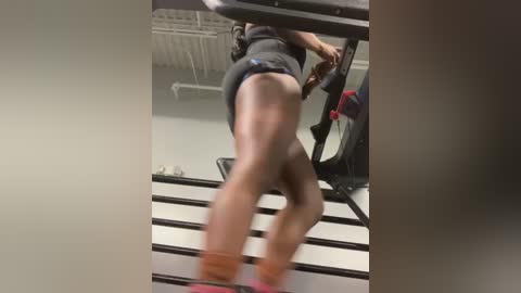 Media: A video of a person in a dark gray athletic outfit, including shorts and a top, climbing a flight of stairs. The image is slightly blurred and taken in an indoor gym setting.