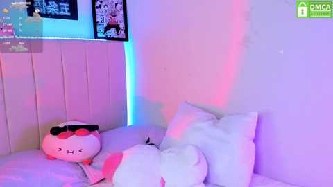 Media: Video of a white bed with a plush, pink pig and two white pillows, illuminated by soft, multicolored LED lights, creating a serene, pastel-lit bedroom atmosphere.