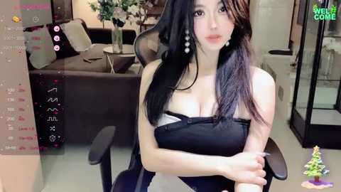 Media: Video of an East Asian woman with long black hair, wearing a black strapless top, sitting on a chair in a modern living room.