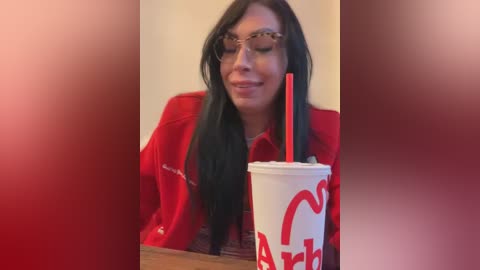 Media: A video of a woman with long, straight black hair, wearing glasses and a red shirt, holding a McDonald's drink with a red straw, smiling.