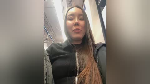 Media: Video of a young woman with long brown hair, wearing a black jacket, seated in a subway car. The background shows the train's interior with metallic panels and blue lighting.