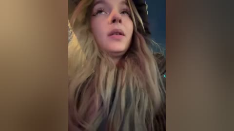 Media: Video of a young woman with long, blonde hair, wearing a black and grey hat and coat, looking up with a slightly surprised expression.